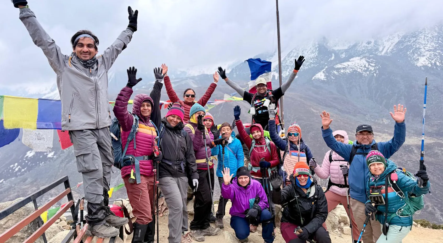 Trekking group celebrating with hands raised amid Himalayan prayer flags